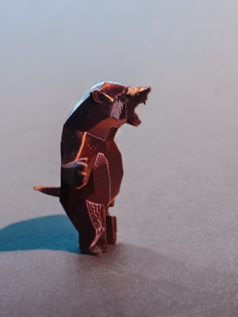 A small, robot-like figure of a bear standing on a flat surface with its mouth open, facing to the right.