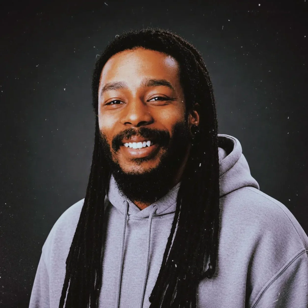 A smiling Robert Jordan with long dreadlocks, a beard, and mustache wearing a gray hoodie.