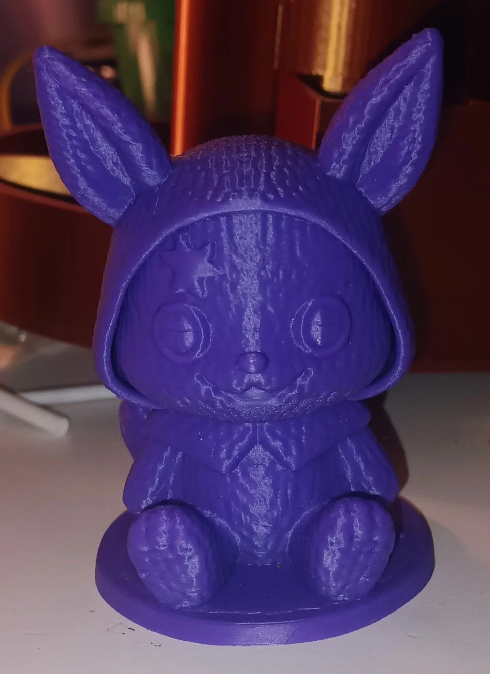 Purple 3D-printed figurine of a cute animal, possibly a bunny or a fox, with large ears and big round eyes, sitting on a small round base.