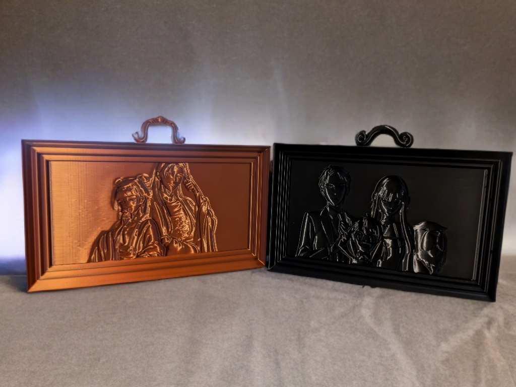 Two framed embossed metal plaques, one in copper color and the other in black, depicting scenes with people. The copper plaque shows two individuals, possibly adults and children, and the black plaque shows two women and a dog.