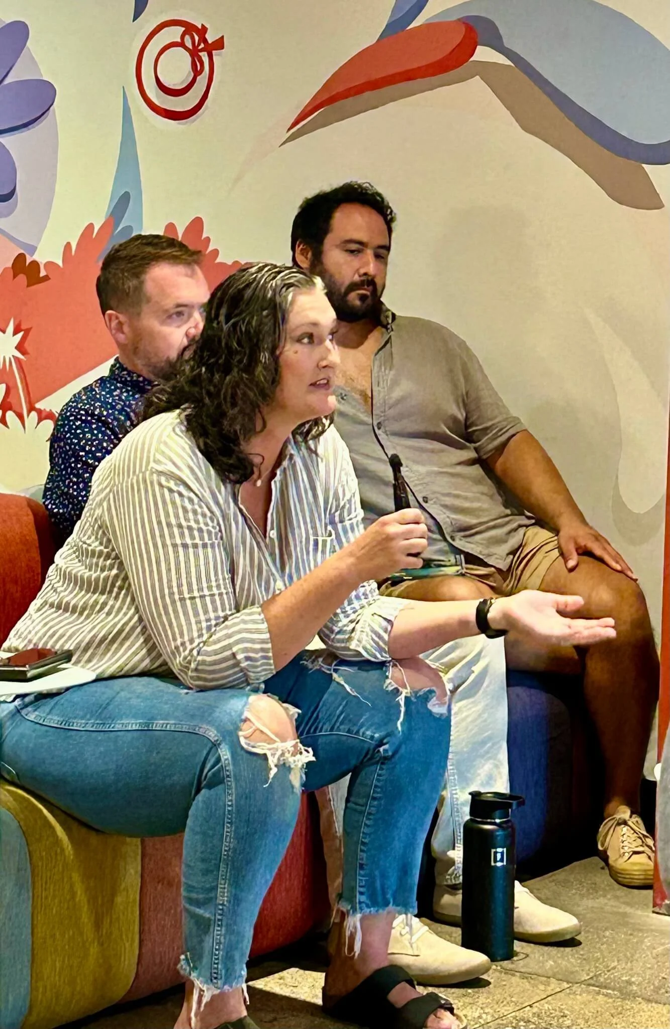 A woman holding a microphone while sitting on a sofa with two men in front of a colorful wall at Central Avenue Church in Pasadena, California