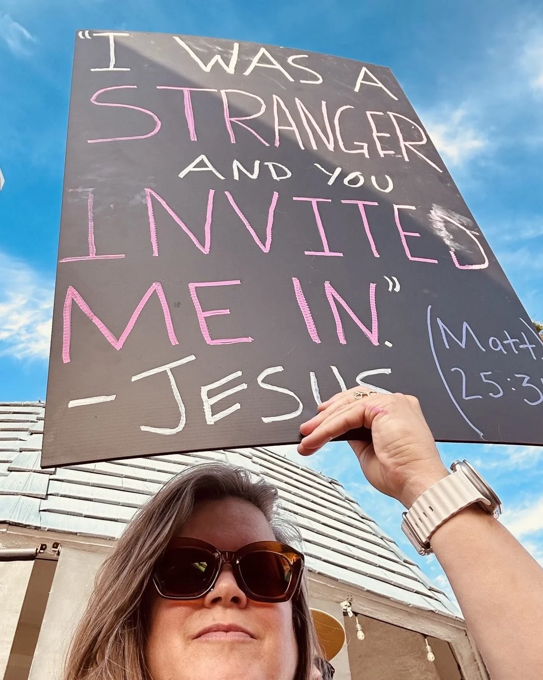 Julie Davis of Central Avenue Church in Pasadena holding up a sign at a protest that says "I was a stranger and you invited me in. – Jesus"