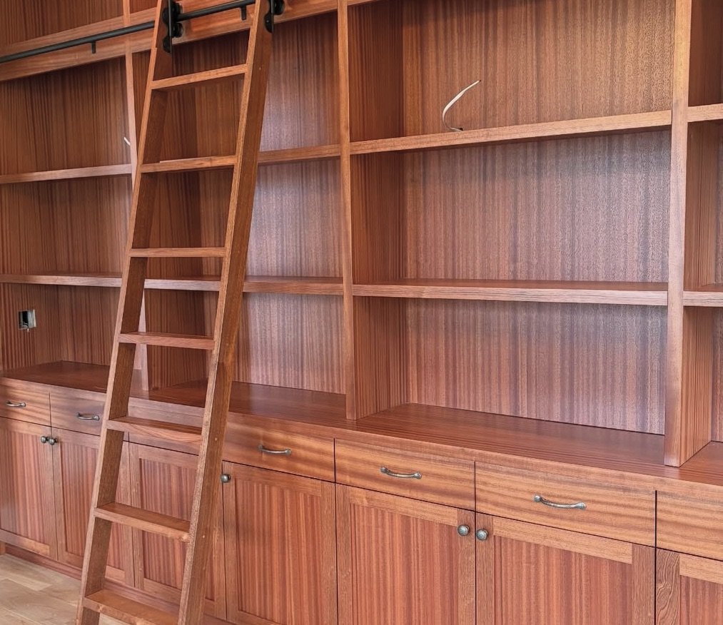 Empty wooden built-in shelves with a ladder leaning against them in a room.