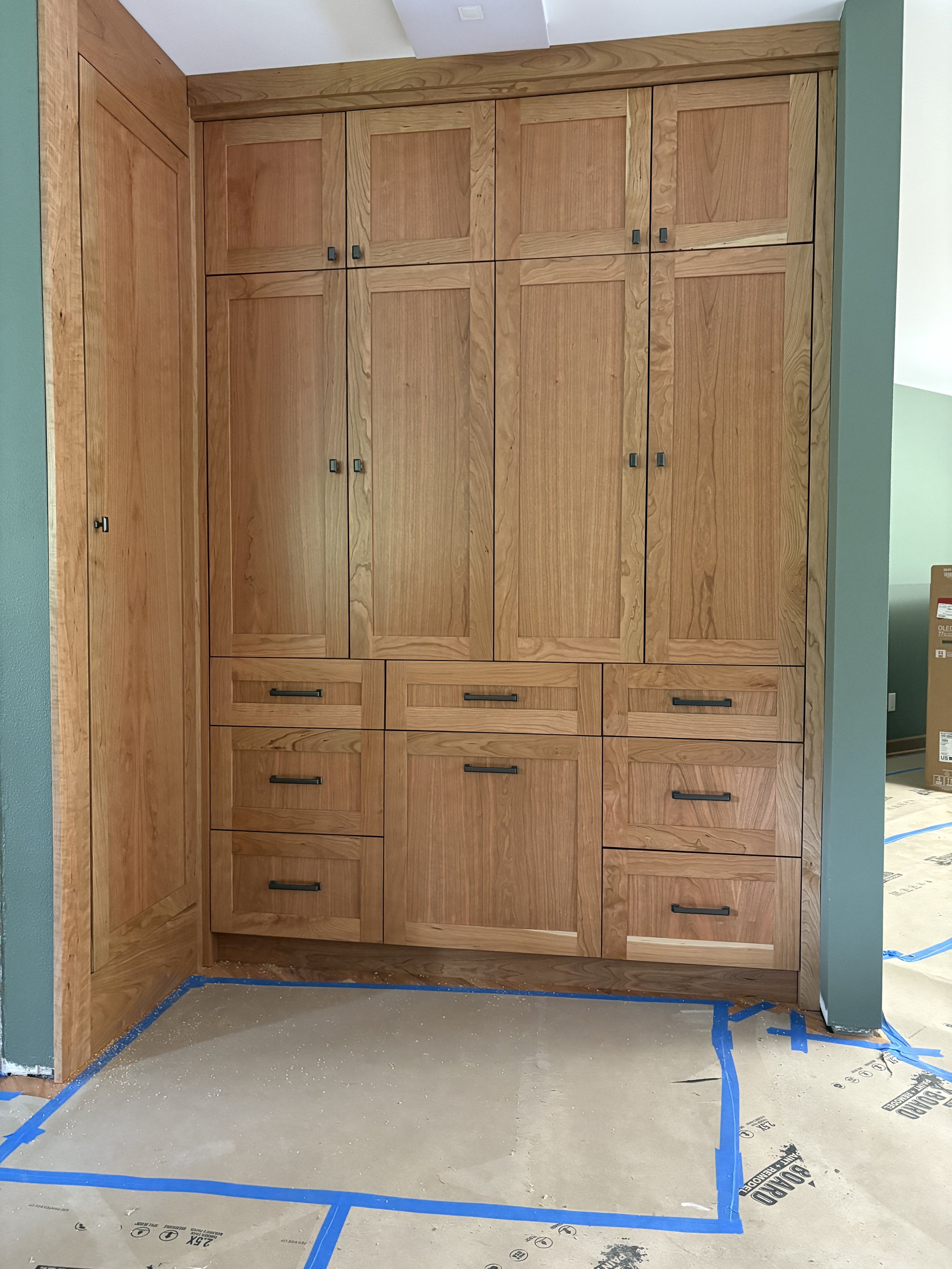 Wooden built-in cabinets with black handles in a room under construction, taped floor.