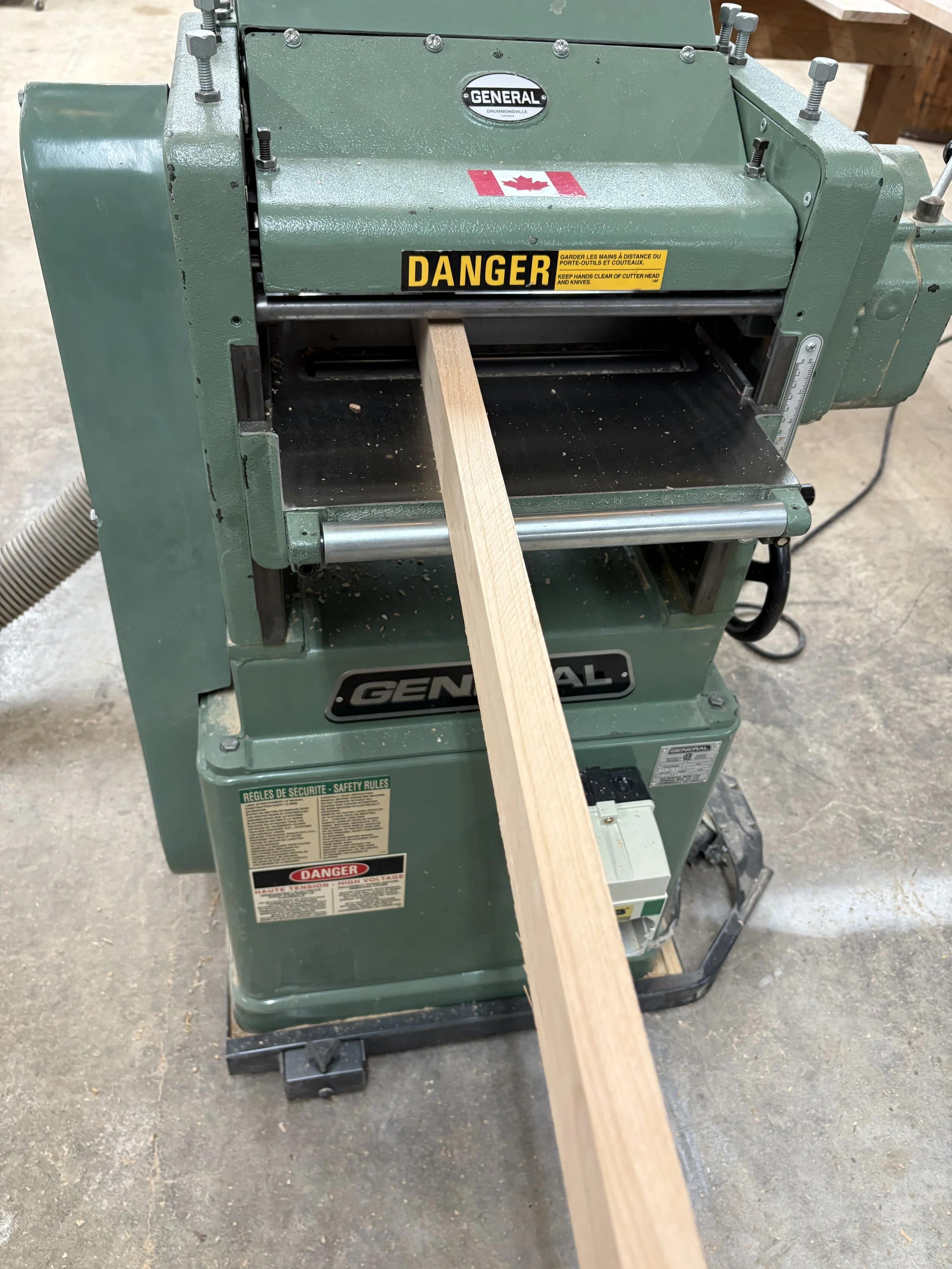 Green woodworking jointer machine with a piece of wood being fed through, positioned in a workshop.
