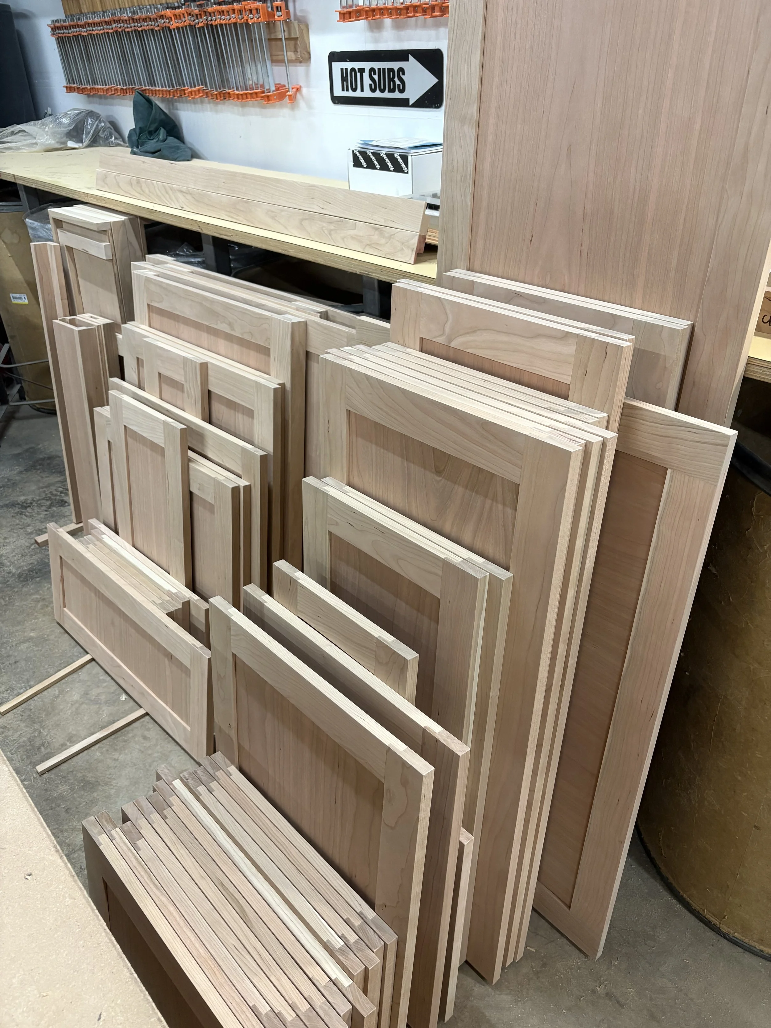 A variety of unfinished wooden cabinet doors and frames leaning against a wall in a woodworking shop.