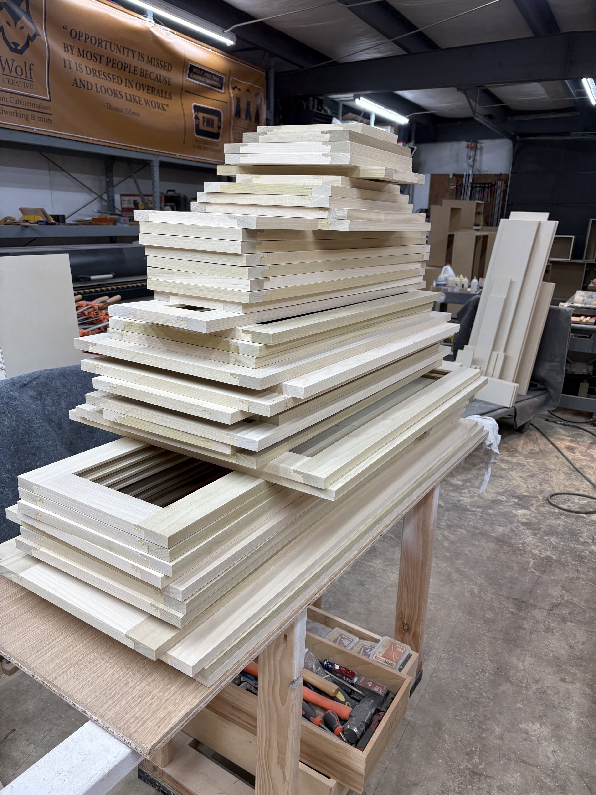 Stacked unfinished wooden picture frames and trim pieces on a workbench in a woodworking shop.