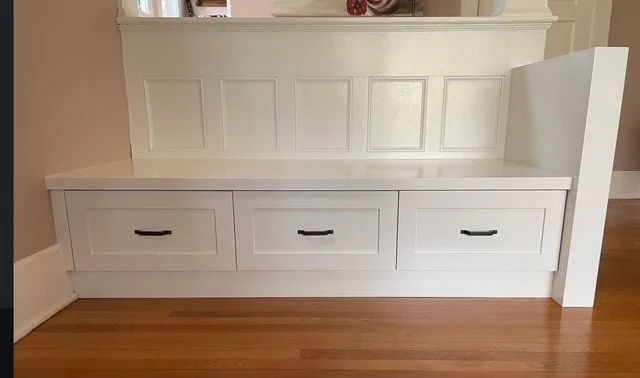 White built-in bench with drawers and panel detailing in a room with hardwood flooring.