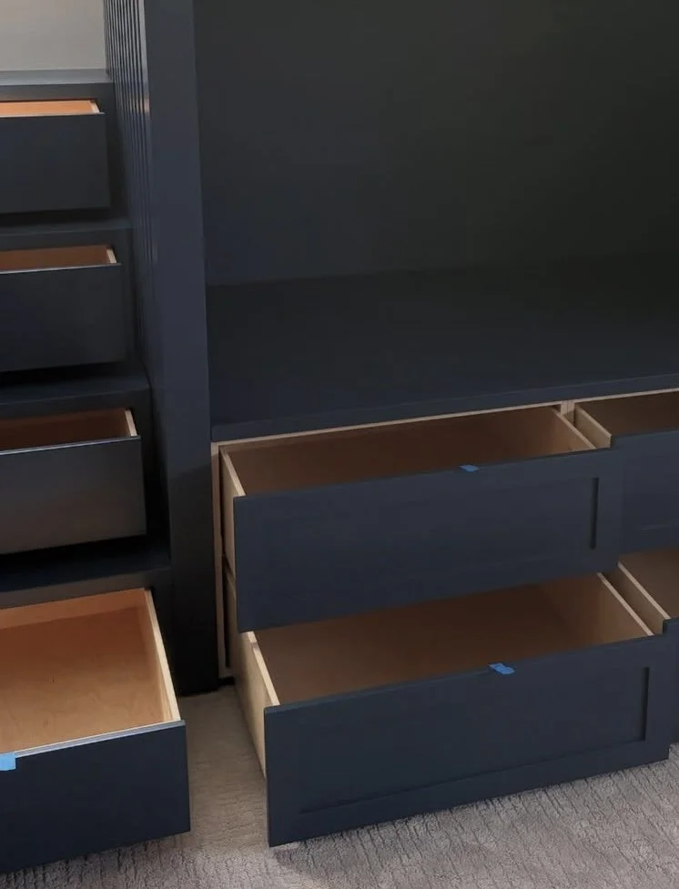 Multiple empty black and natural wood-colored drawers in a dark blue cabinet or shelving unit.