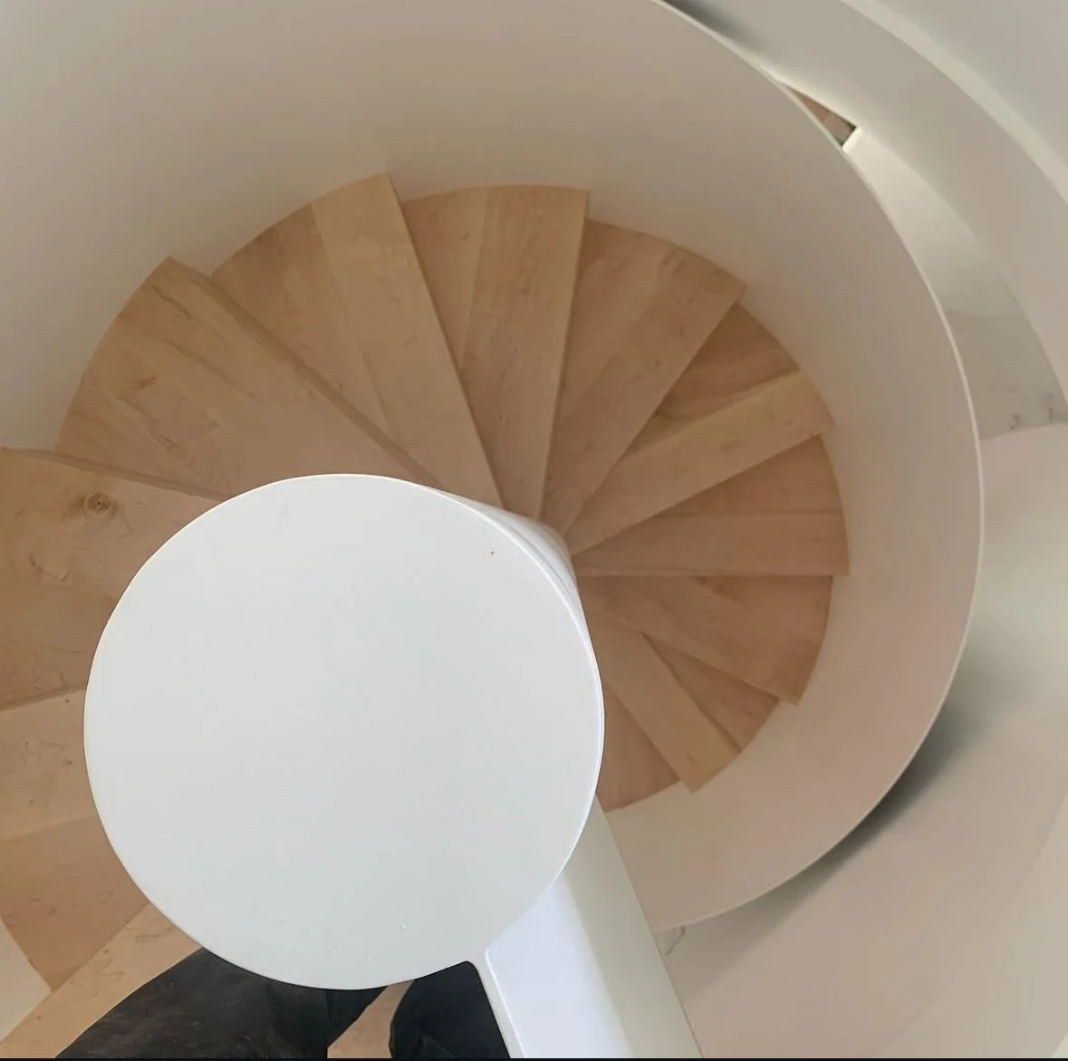 A spiral staircase viewed from above, with wooden steps and a white handrail.