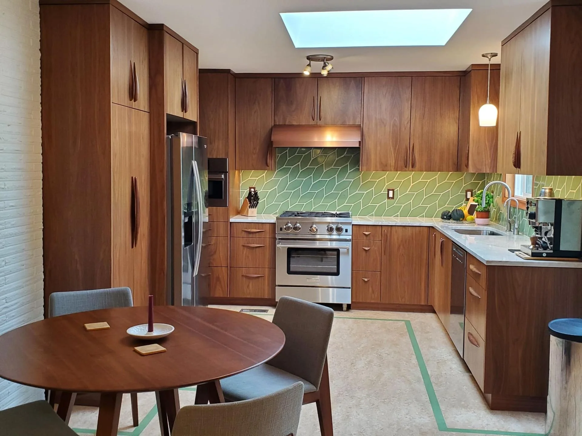 A cozy kitchen with oak cabinets, stainless steel appliances, green geometric tile backsplash, and a small round dining table with four chairs.