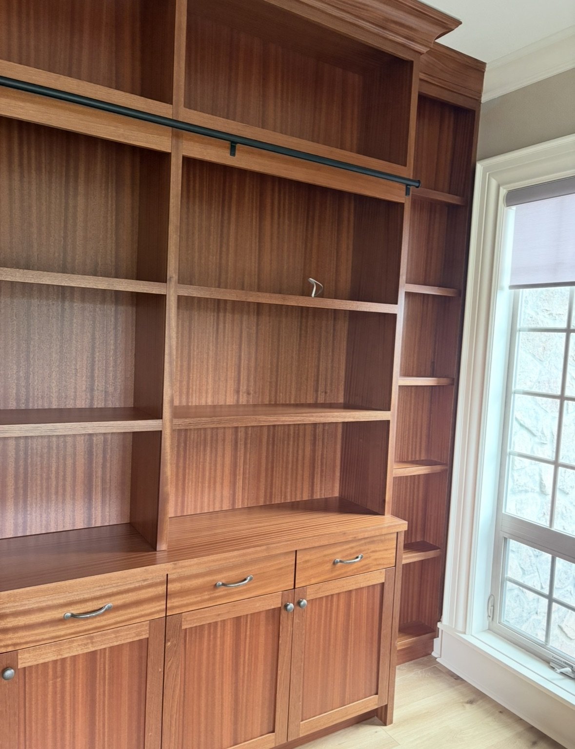 Empty wooden shelving unit with drawers next to a window.