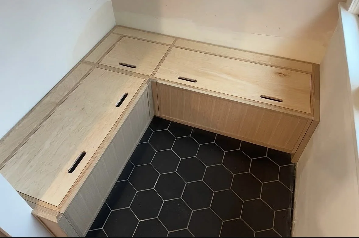 Corner wooden bench with storage drawers and black hexagonal floor tiles.