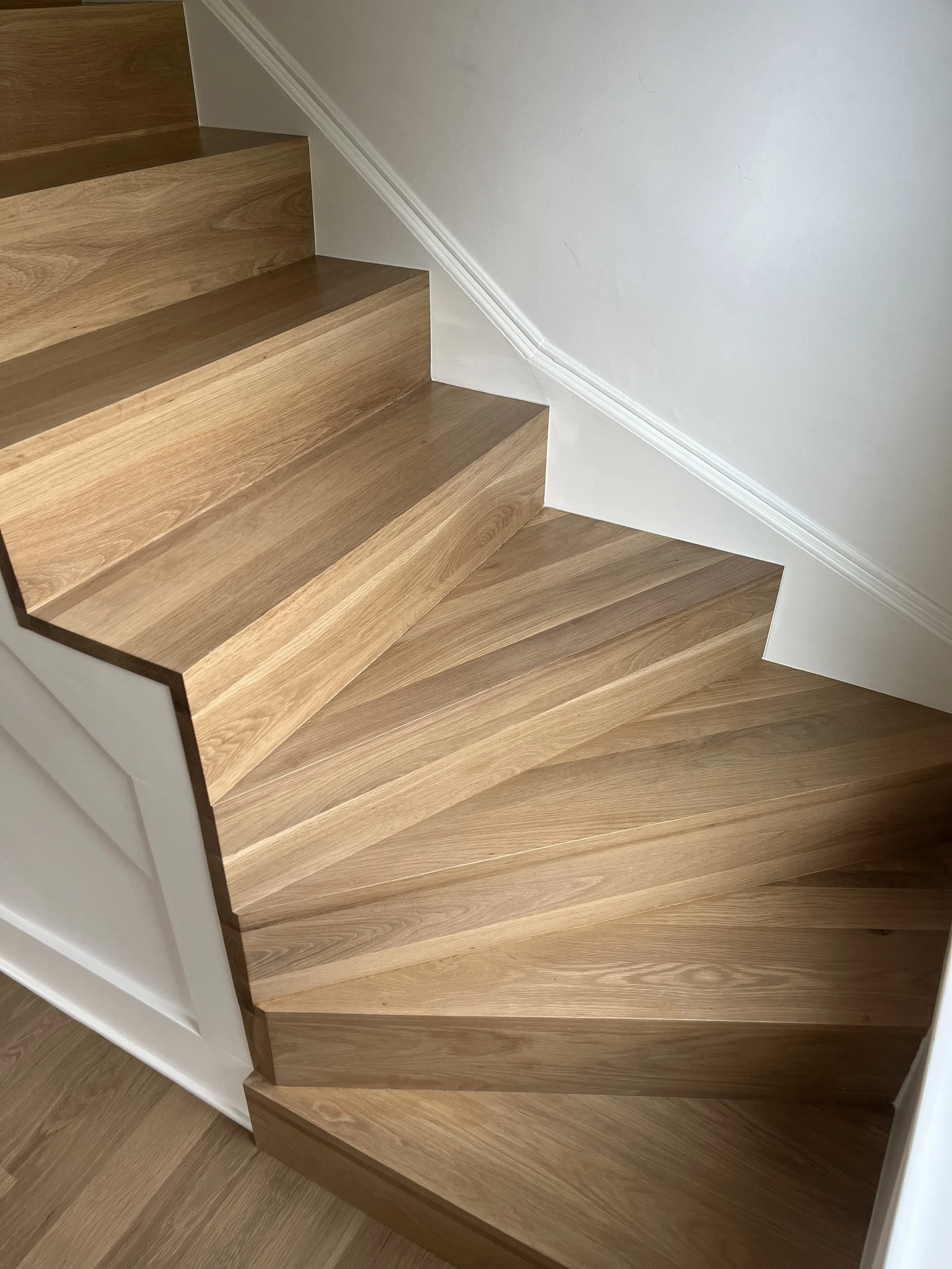 Photo of a wooden staircase with a white wall and white trim on the side.