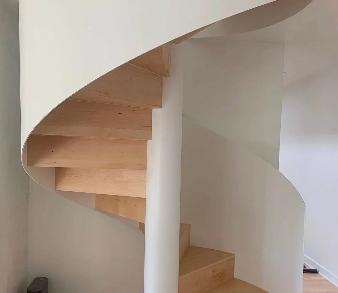 Wooden spiral staircase with white walls surrounding it.