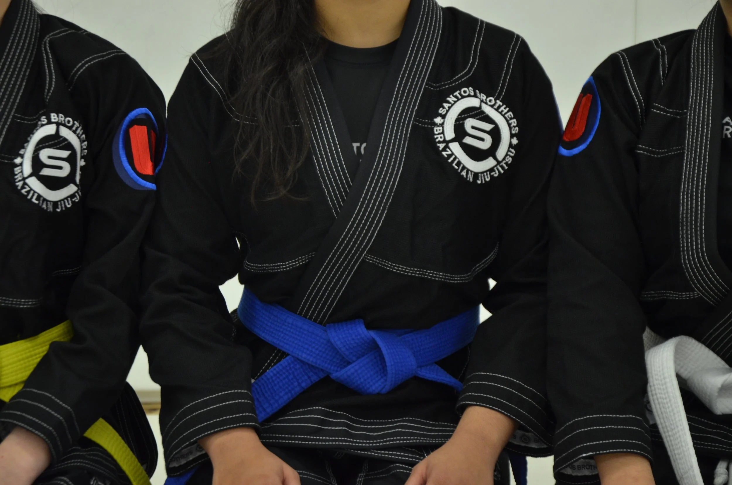 Brazilian Jiu-Jitsu practitioners wearing black gi uniforms with patches and colored belts, including a blue belt.