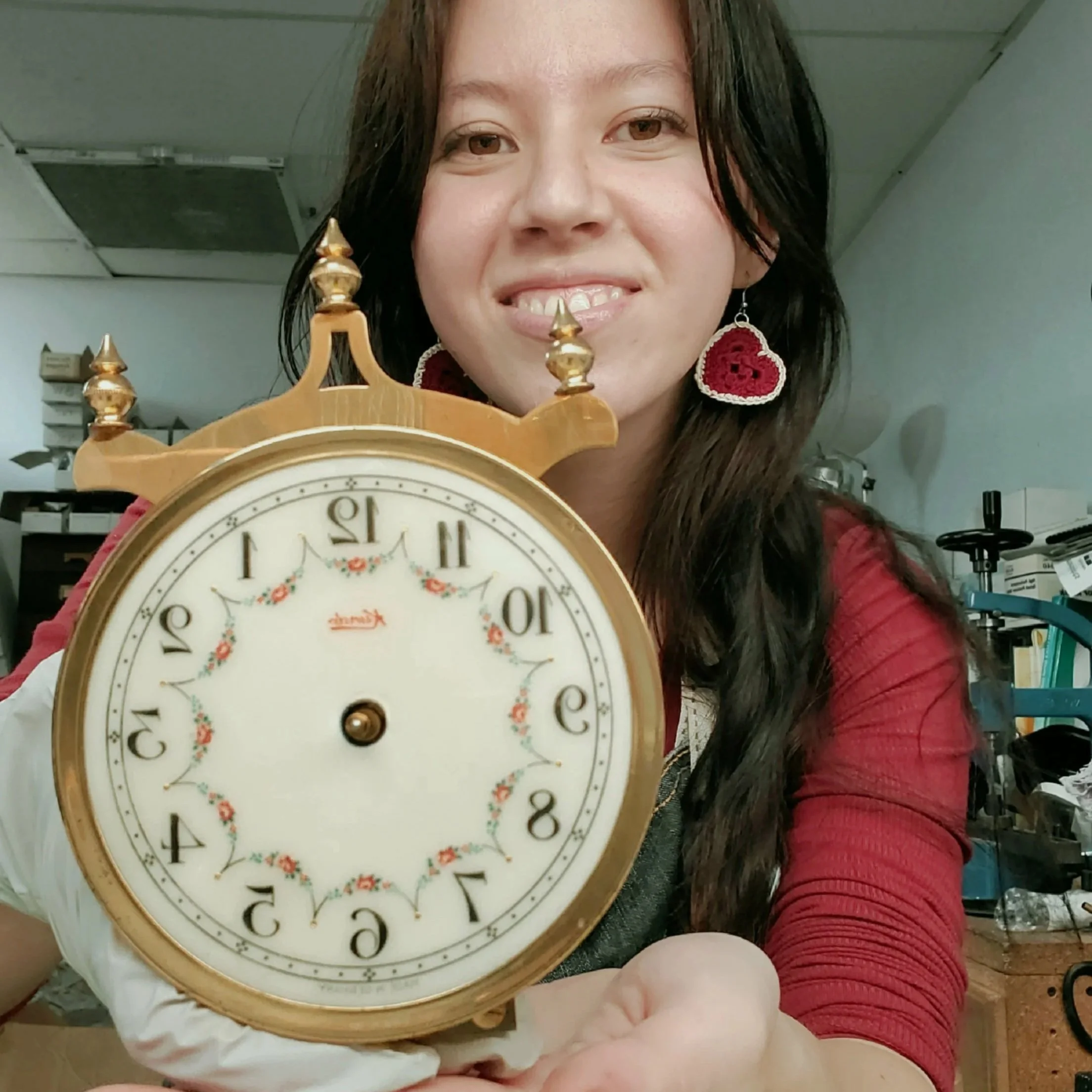 A woman holding a vintage-style clock with a floral design face, smiling at the camera.
