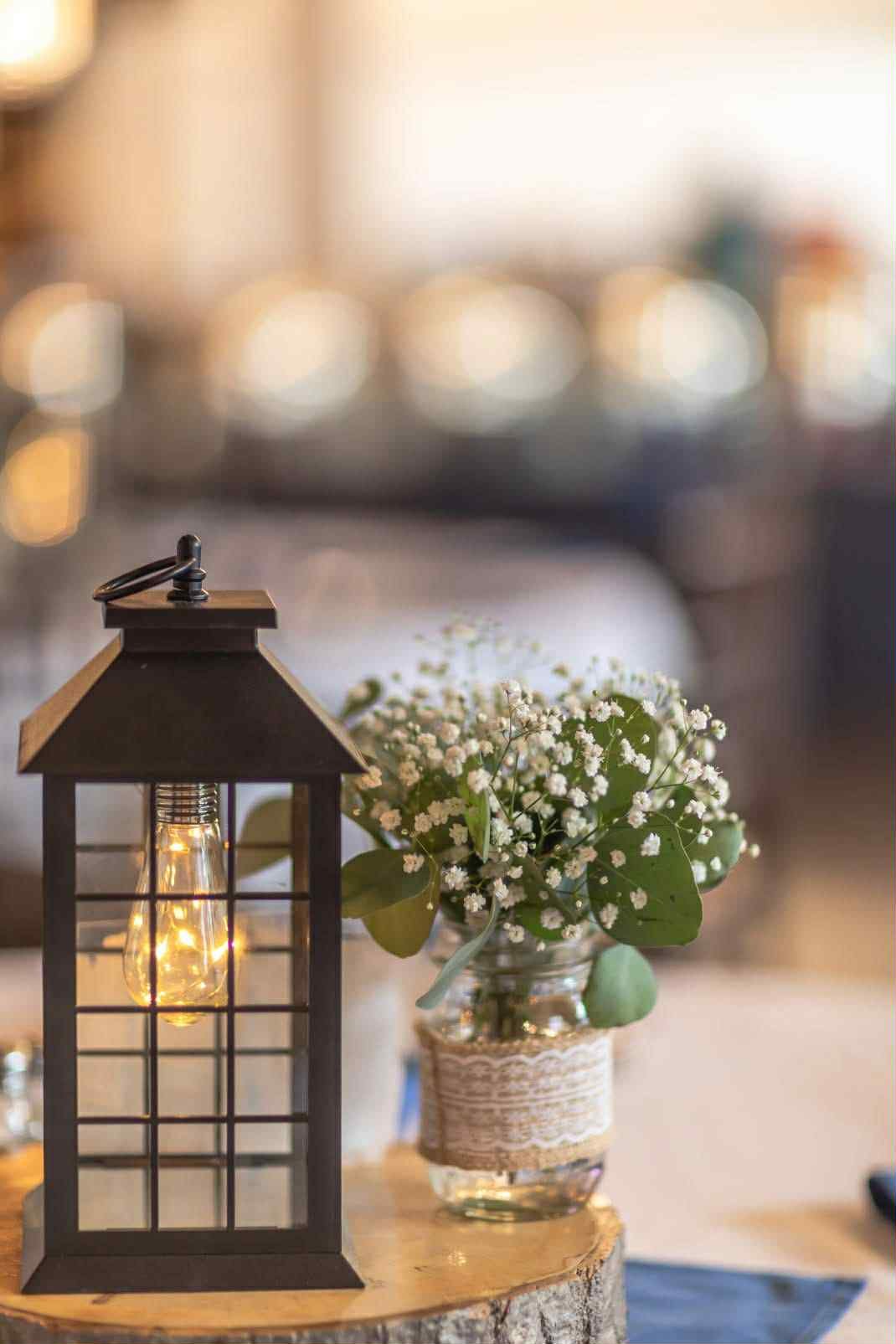 A table with a decorative lantern and a glass jar filled with white baby's breath flowers and green leaves.
