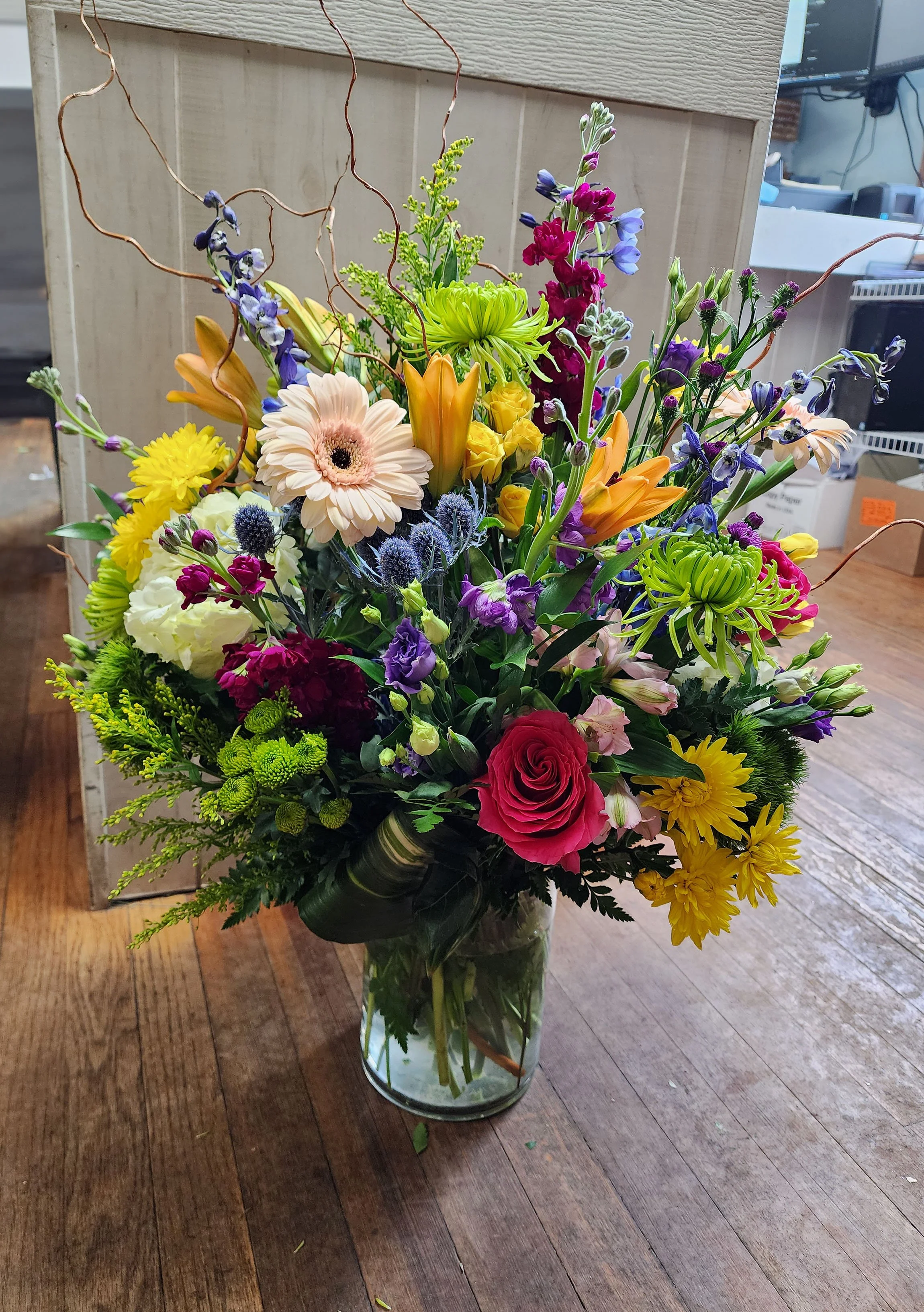 A colorful bouquet of mixed flowers in a glass vase on a wooden table.