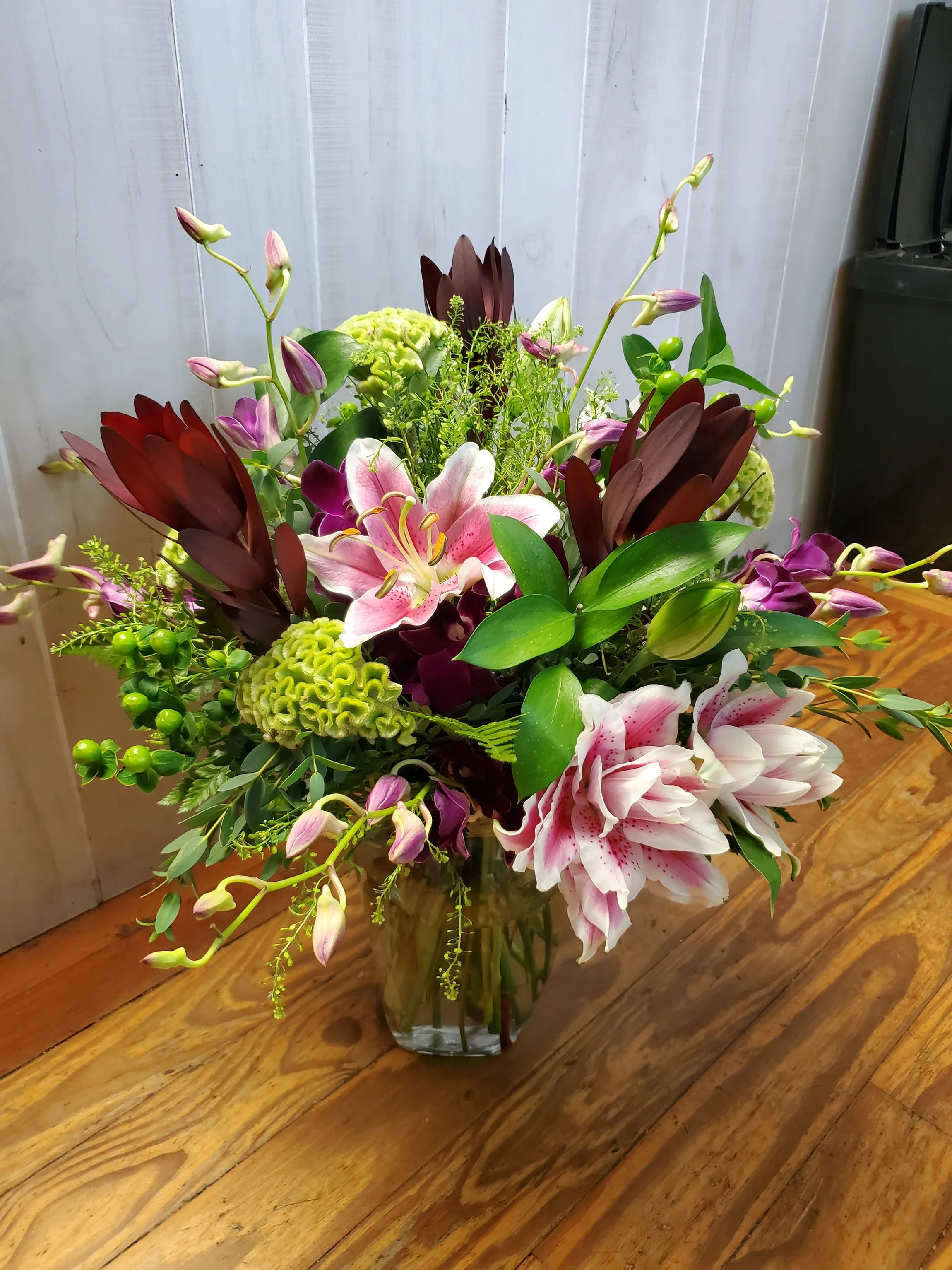 A colorful flower bouquet in a glass vase on a wooden table.
