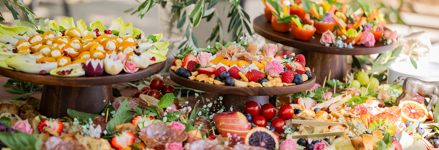 Colorful display of assorted desserts and fruits on a table, with three wooden stands holding a variety of sweet treats and fresh fruits.