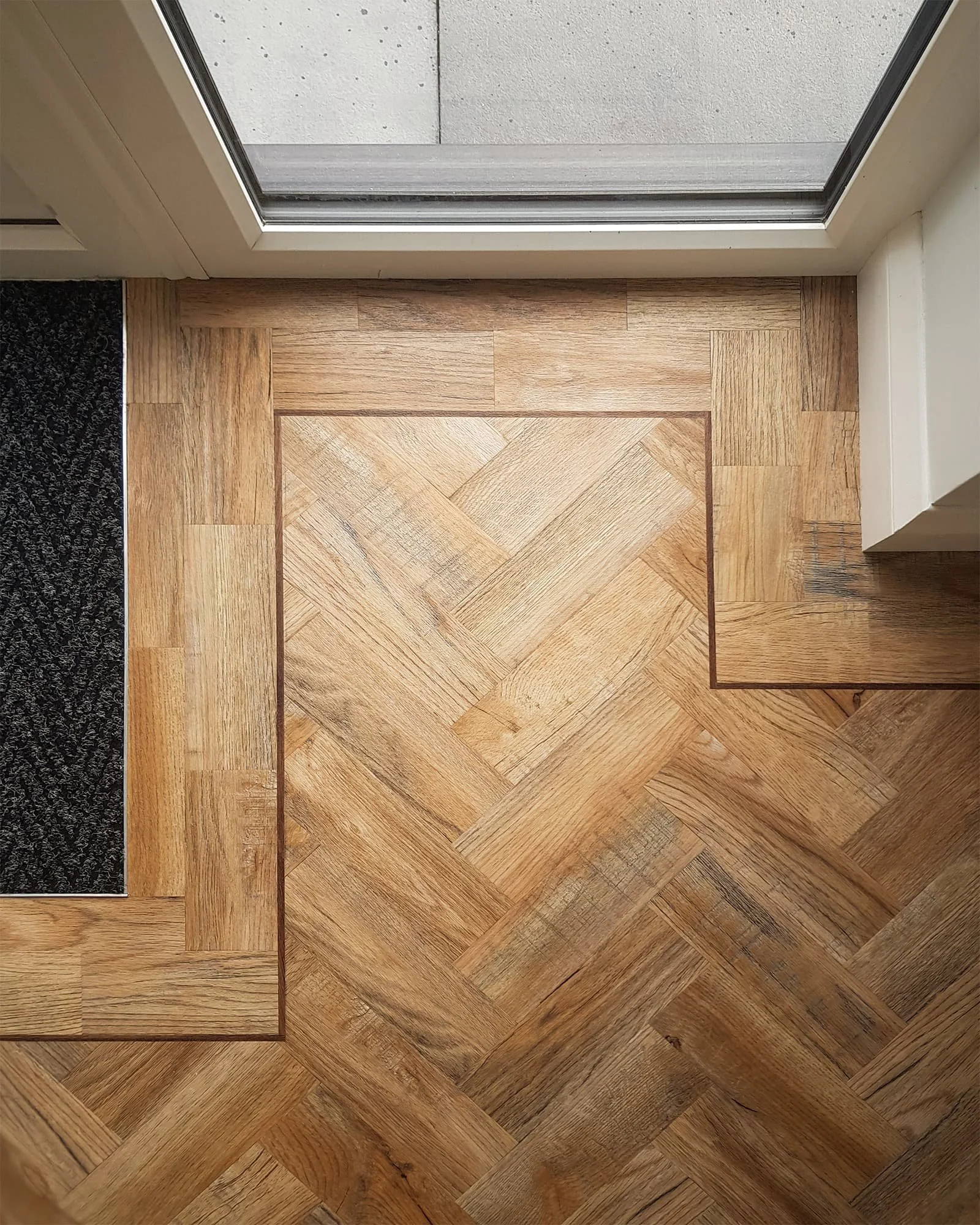 View of a wooden parquet floor next to a sliding glass door leading outside, with a concrete patio visible outside.