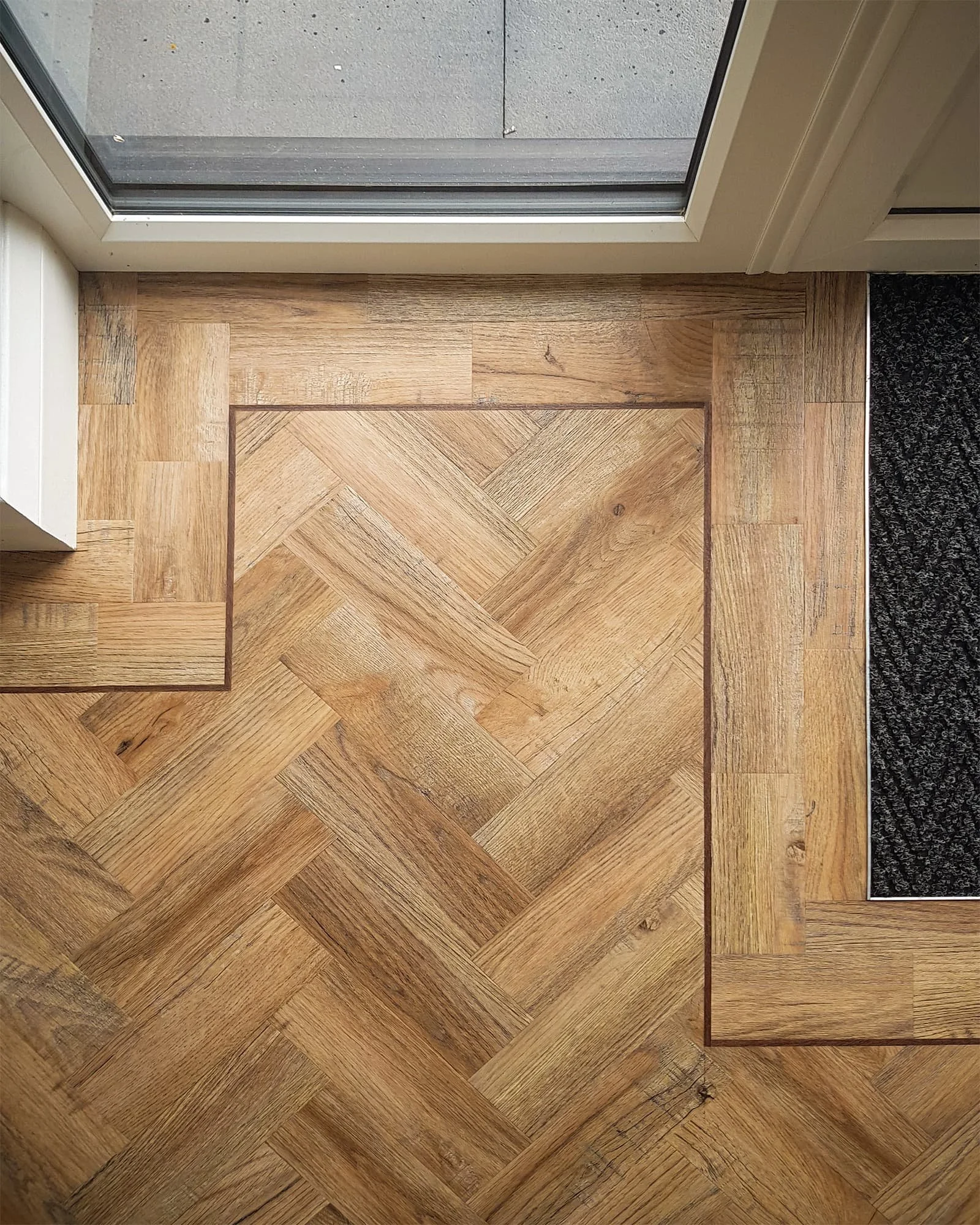 View of a hardwood floor near a sliding glass door with a black rug on the right side.
