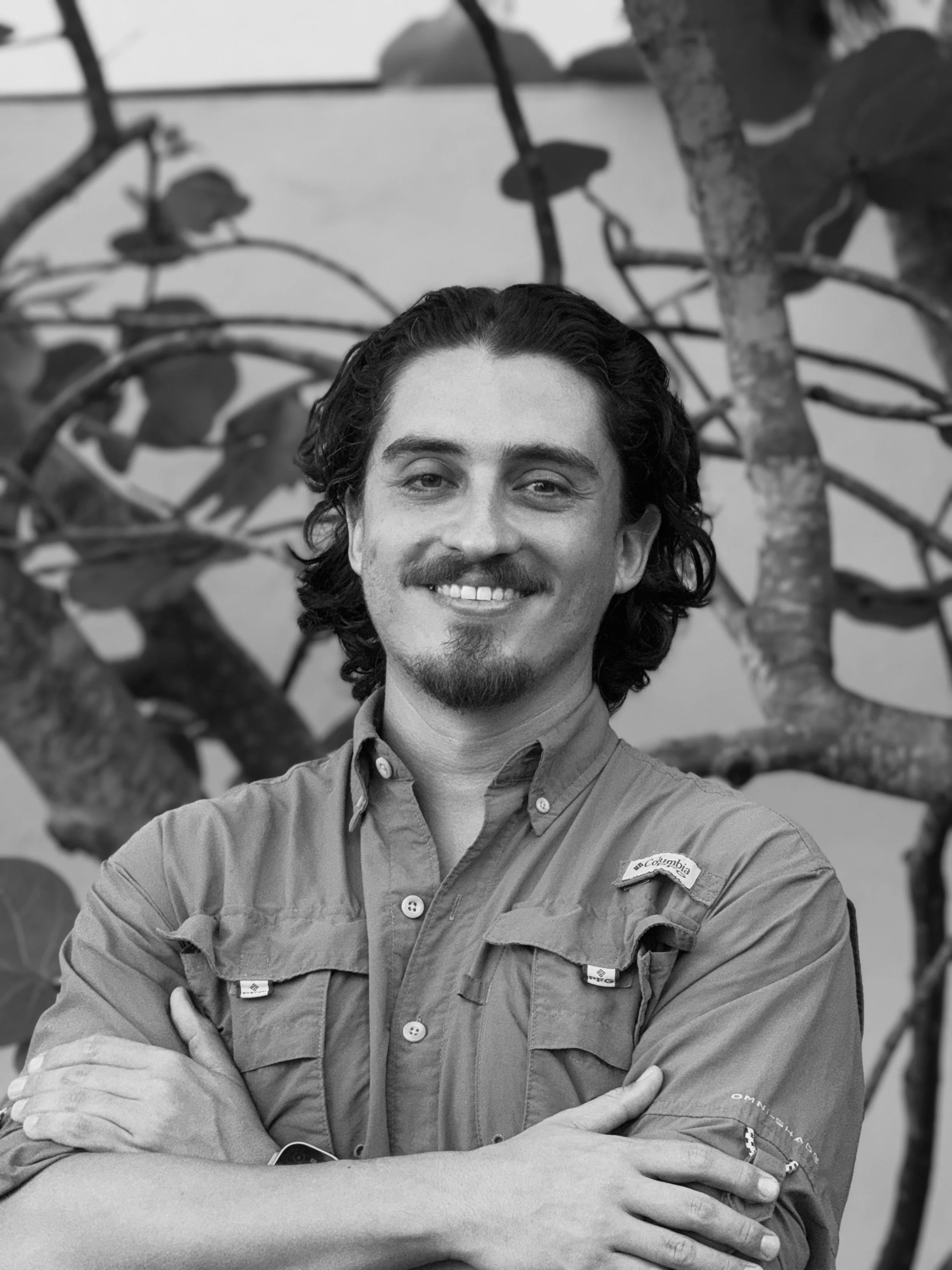 An animated drawing of a smiling man with glasses, a short beard, and short brown hair, outdoors with a blue sky, some clouds, greenery, and water in the background.
