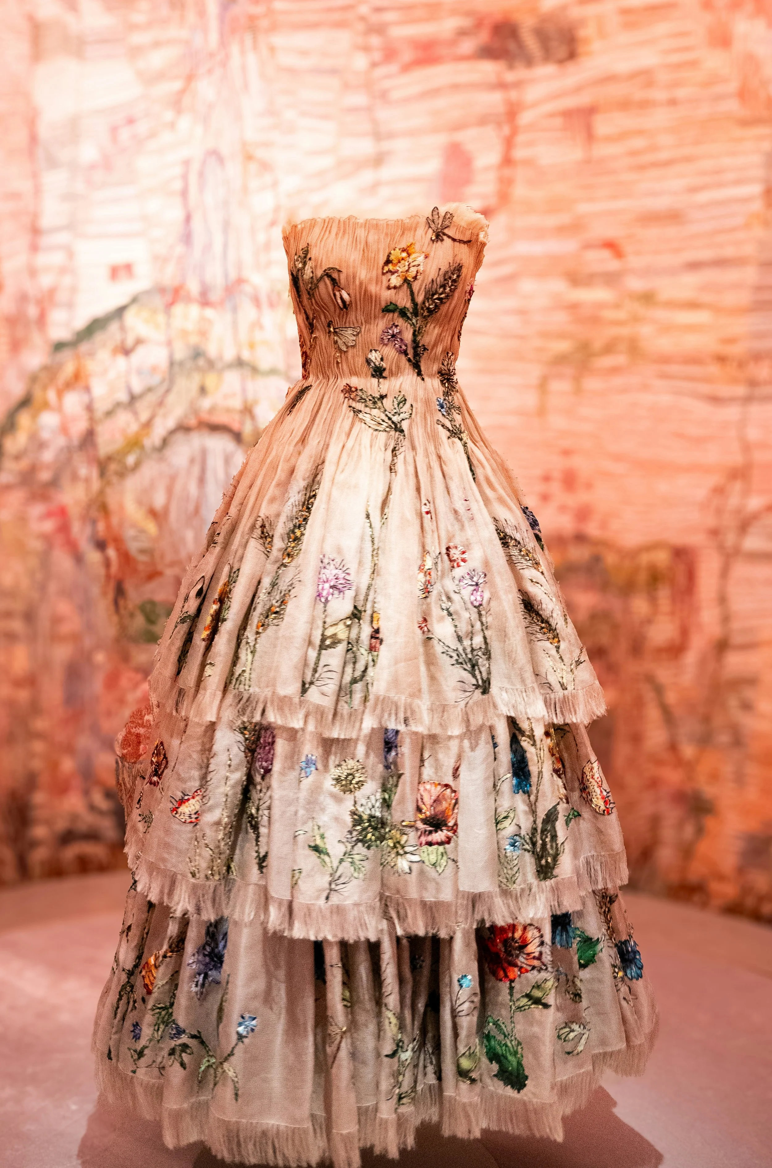 A vintage, strapless, Christian Dior dress with a tiered, floral embroidery design displayed on a mannequin against a textured background.