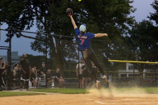 A baseball player  jumping to catch a ball in the outfield during a game, with spectators watching behind a fence.