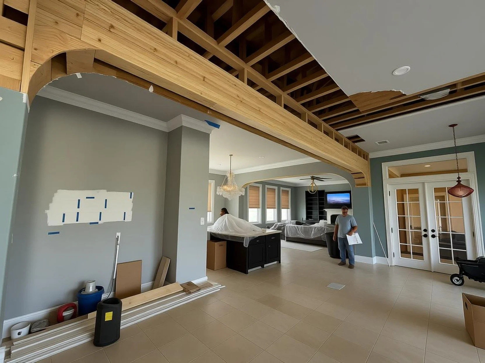 Living room under renovation with construction materials, partially installed wooden ceiling trim, and workers preparing the space.