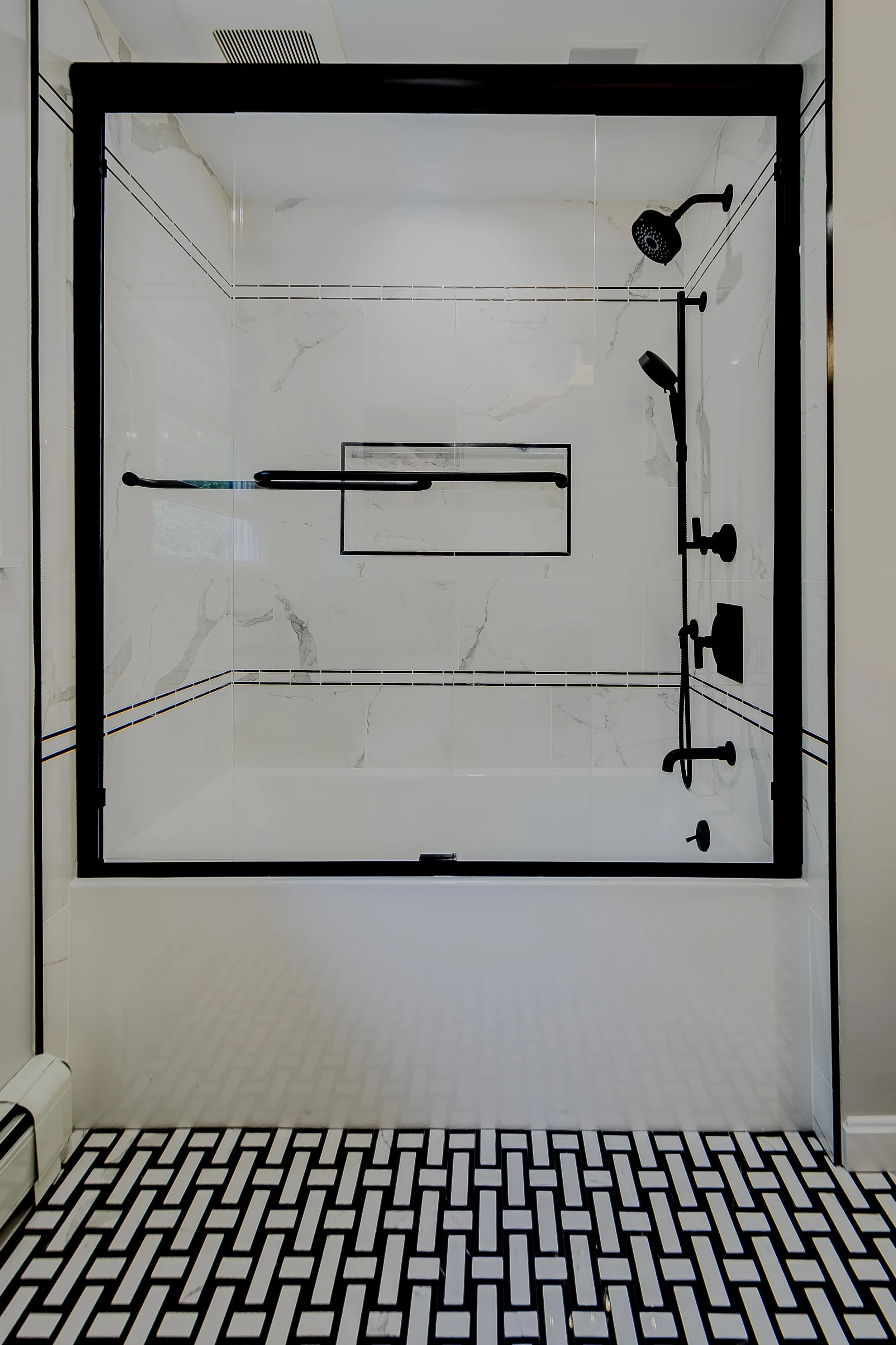 Crisp, clean, and utterly modern. The secondary bathroom's shower area boasts bold black fixtures against pristine veined tile, framed by a striking black grid shower door. It's functional design perfected, adding both style and value.