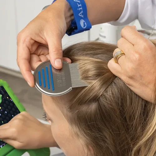 A person getting a haircut, with someone else using a barber comb to style the child's hair, and the child using a tablet.