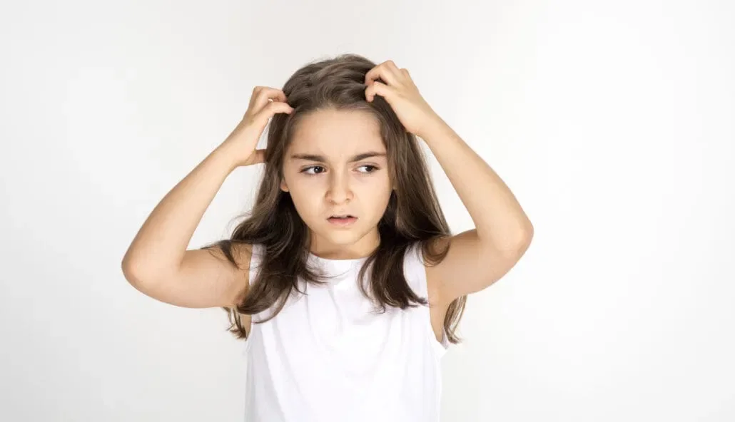 Young girl with long brown hair, wearing a white sleeveless top, holding her head with a confused or distressed expression.