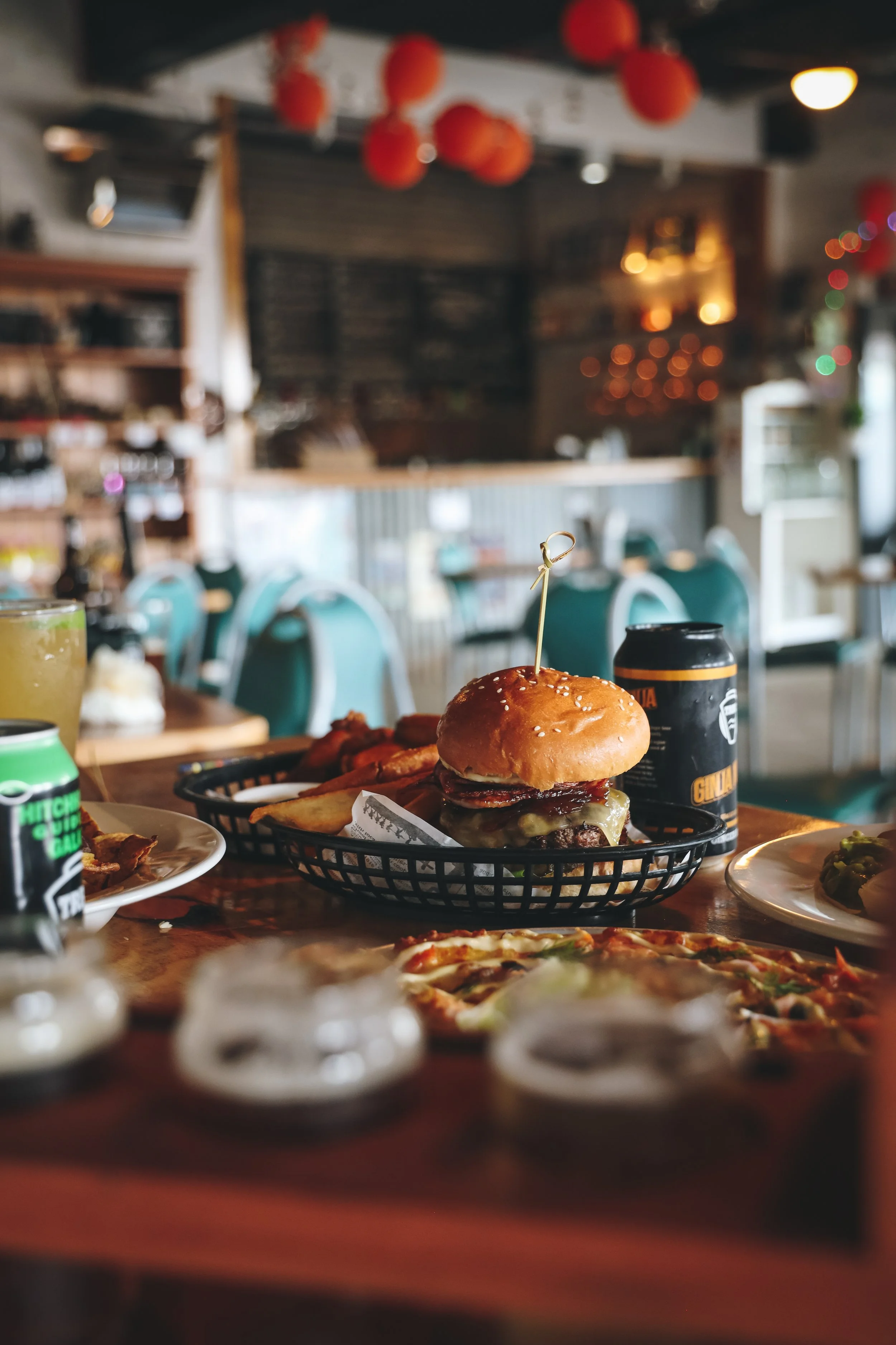 Gourmet burger served in a basket on a café table with drinks and a cozy restaurant background.