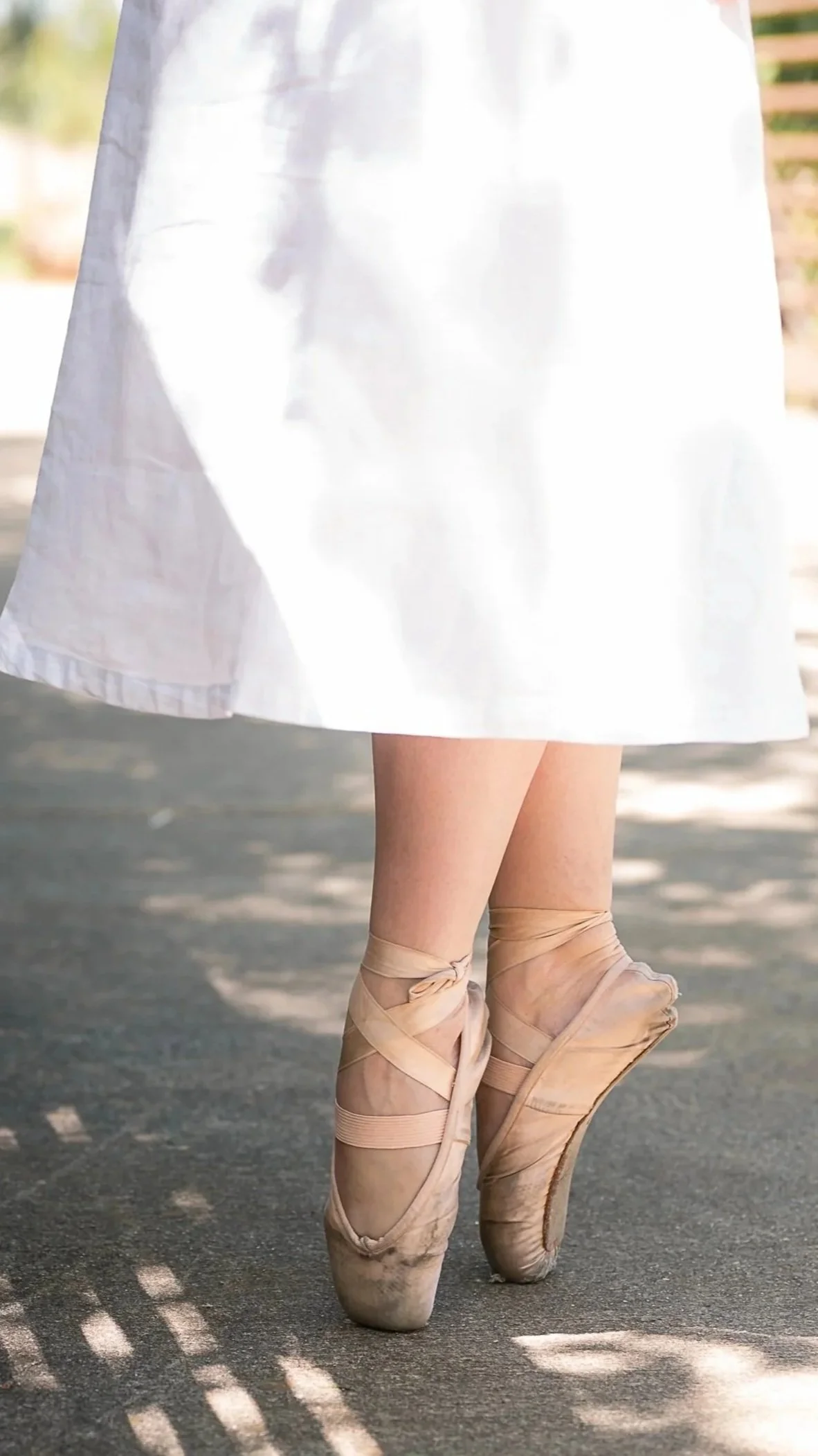 Ballet dancer practicing in pointe shoes wearing a white tutu and standing on her toes on a dance floor.