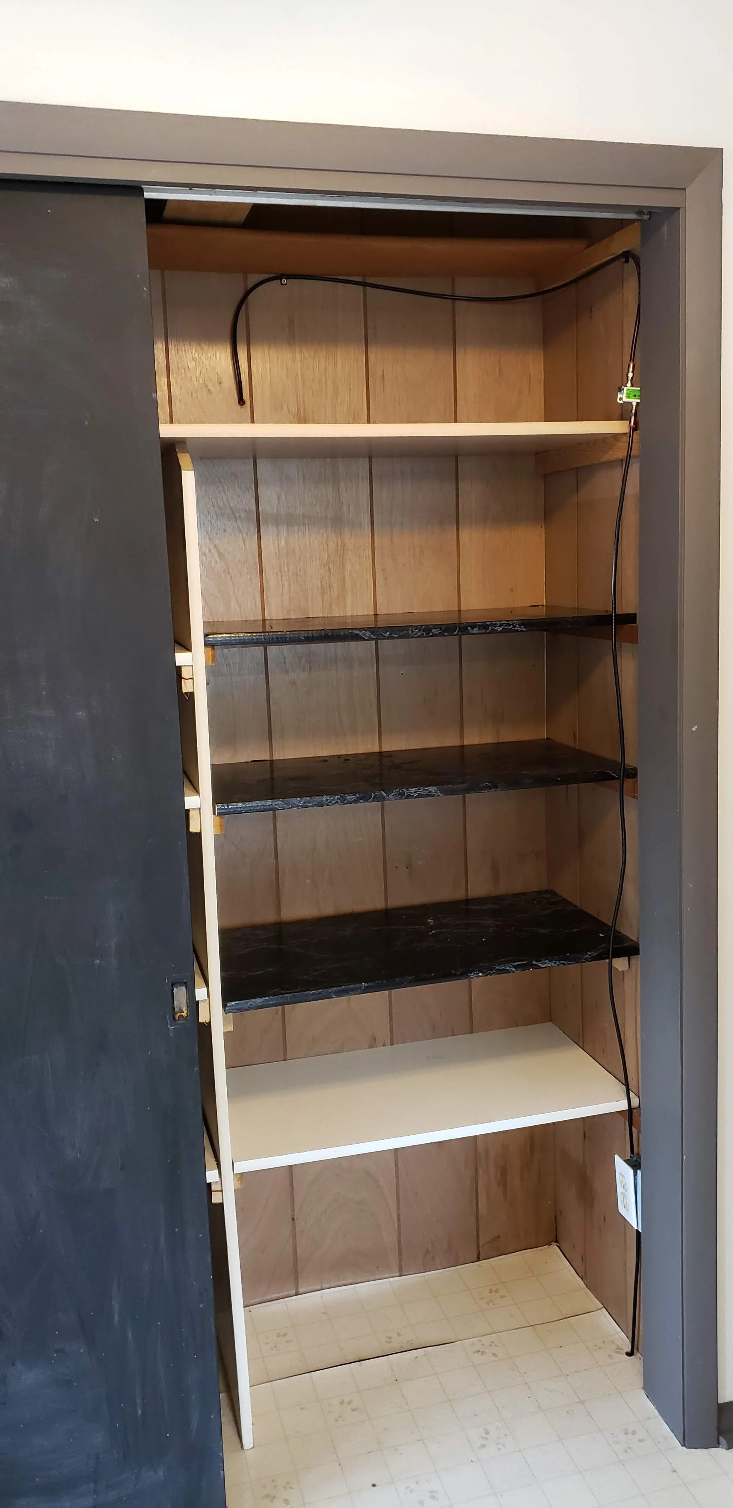 Empty closet with four shelves, one white shelf at the bottom, and dark marble-like shelves above, with a power cord hanging at the top and running down the side.