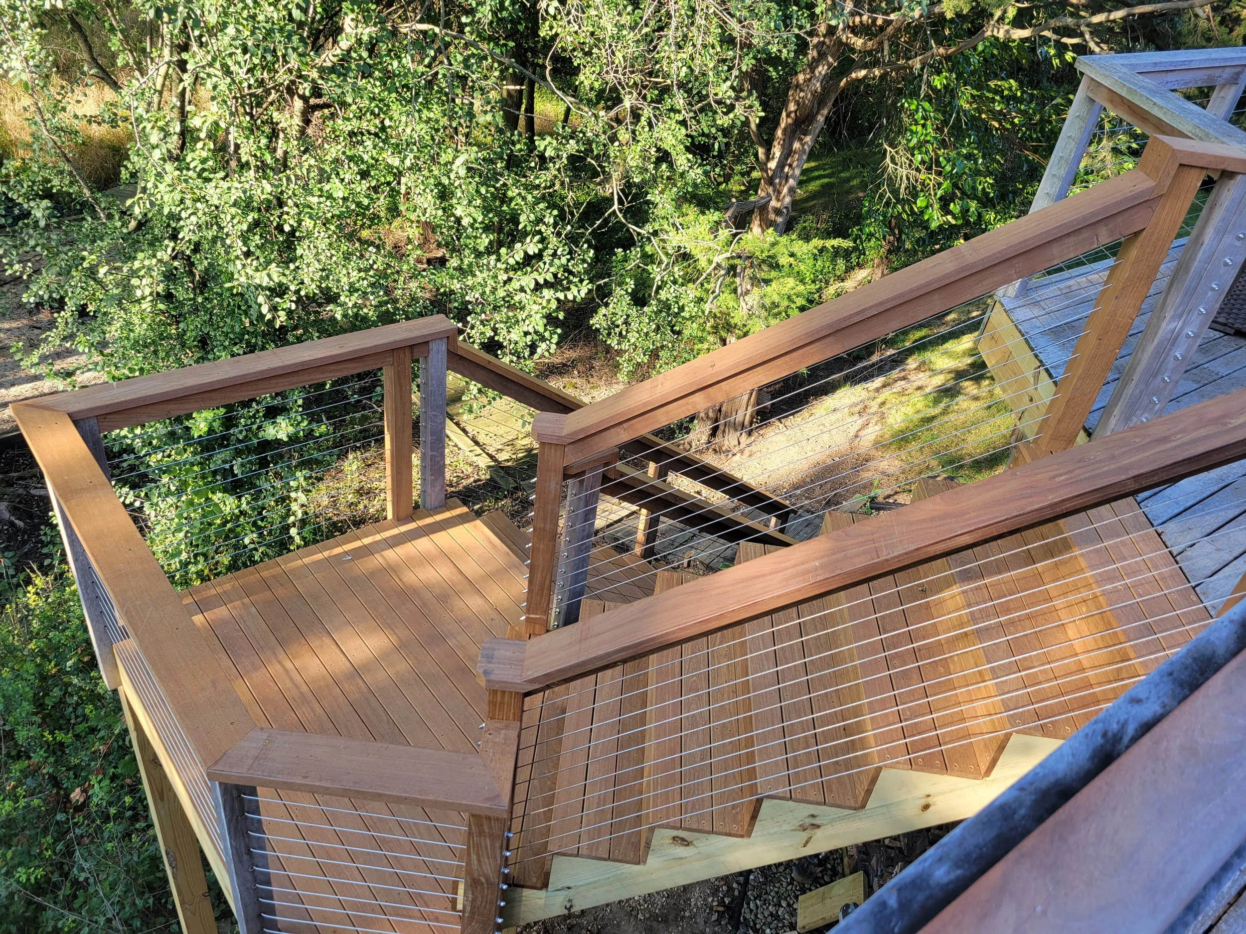 Newly built wooden outdoor staircase with wire railing, surrounded by green trees and shrubs.