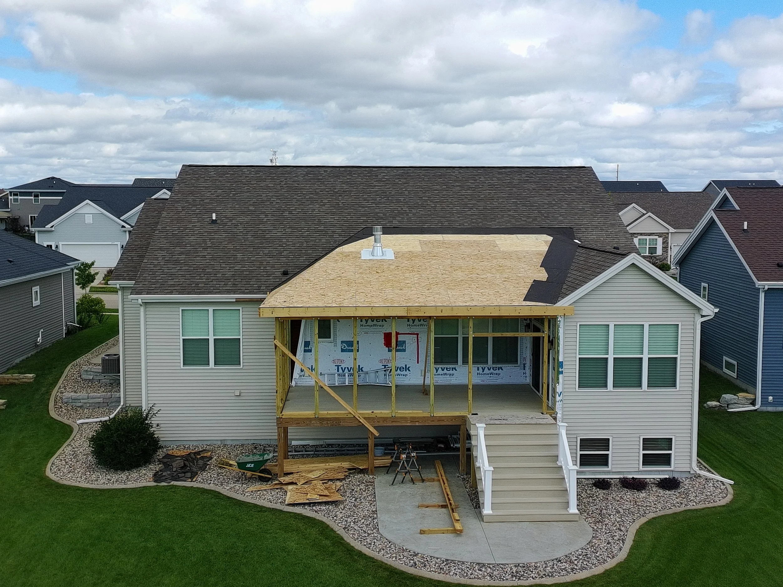 Back of a house under construction with a new deck being built and surrounded by landscaping.