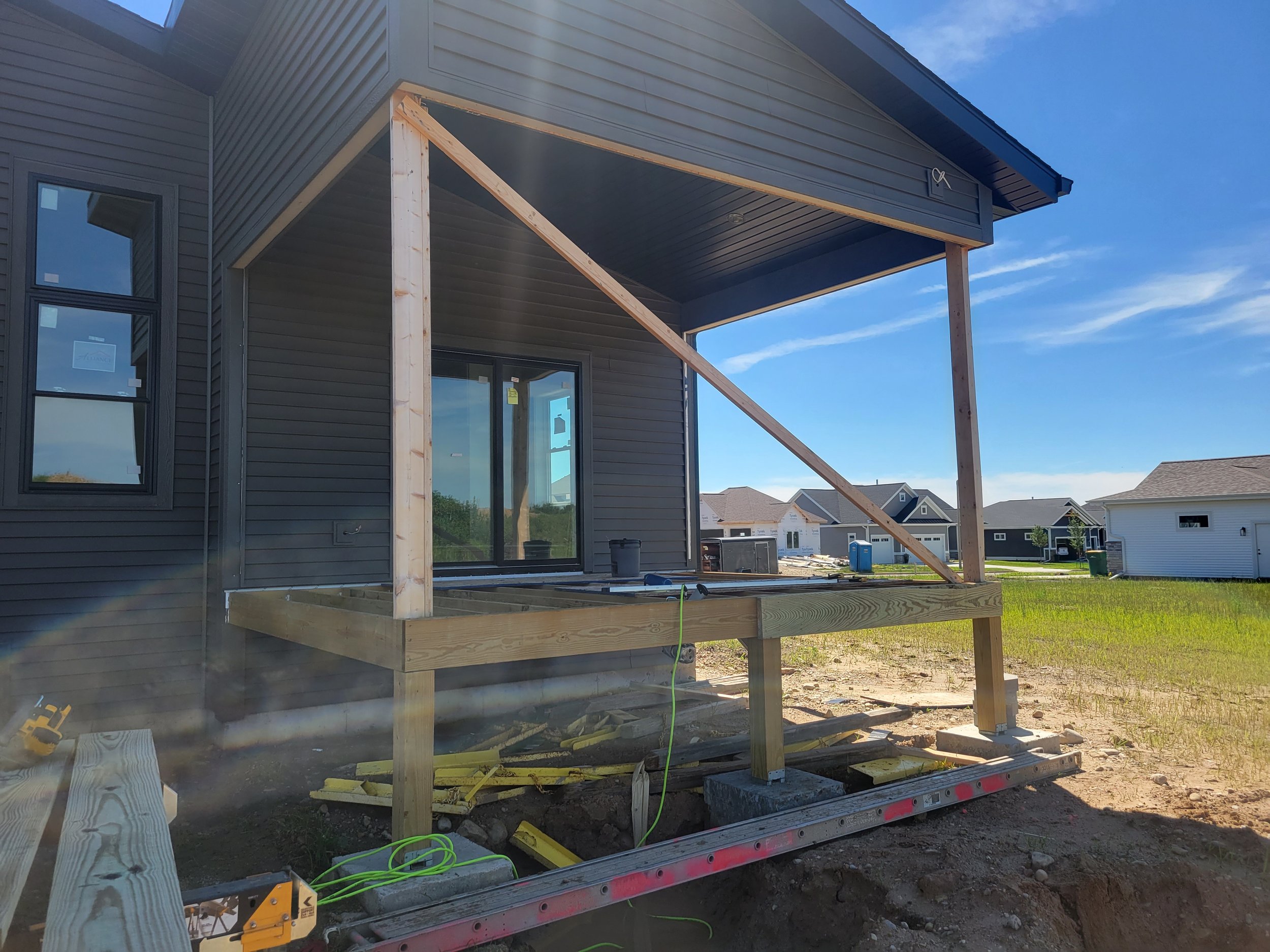 Under construction porch with wooden frame attached to the back of a gray house.