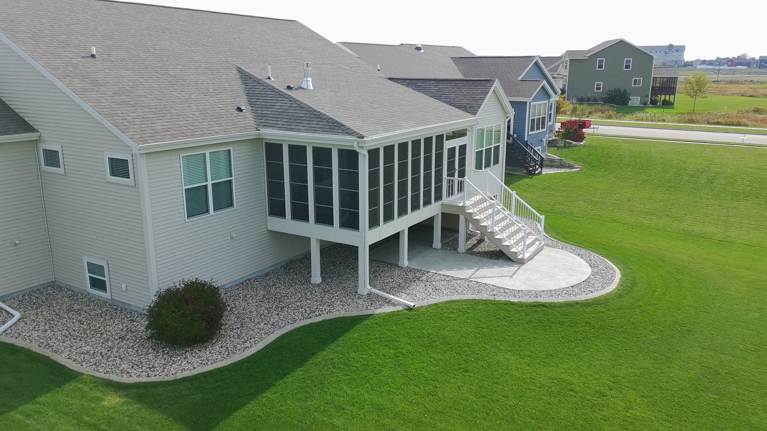 A backyard view of a house with a screened-in porch, white stairs, and a well-maintained green lawn.
