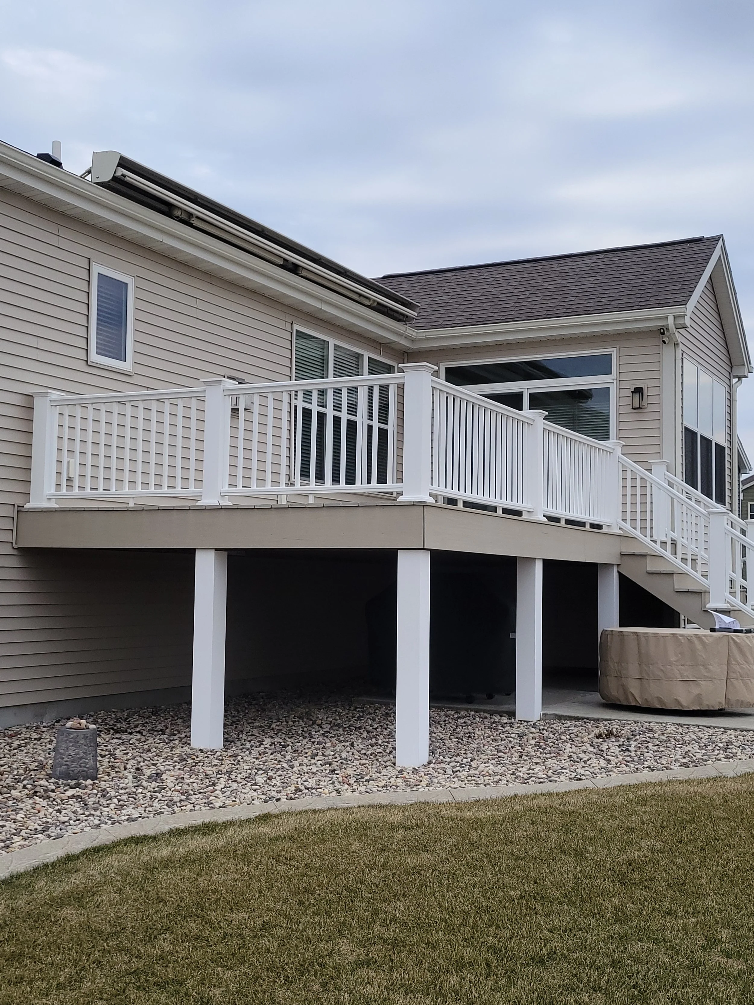Back of house with a raised wooden deck and white railing, stairs leading down, window, and siding, on a cloudy day.