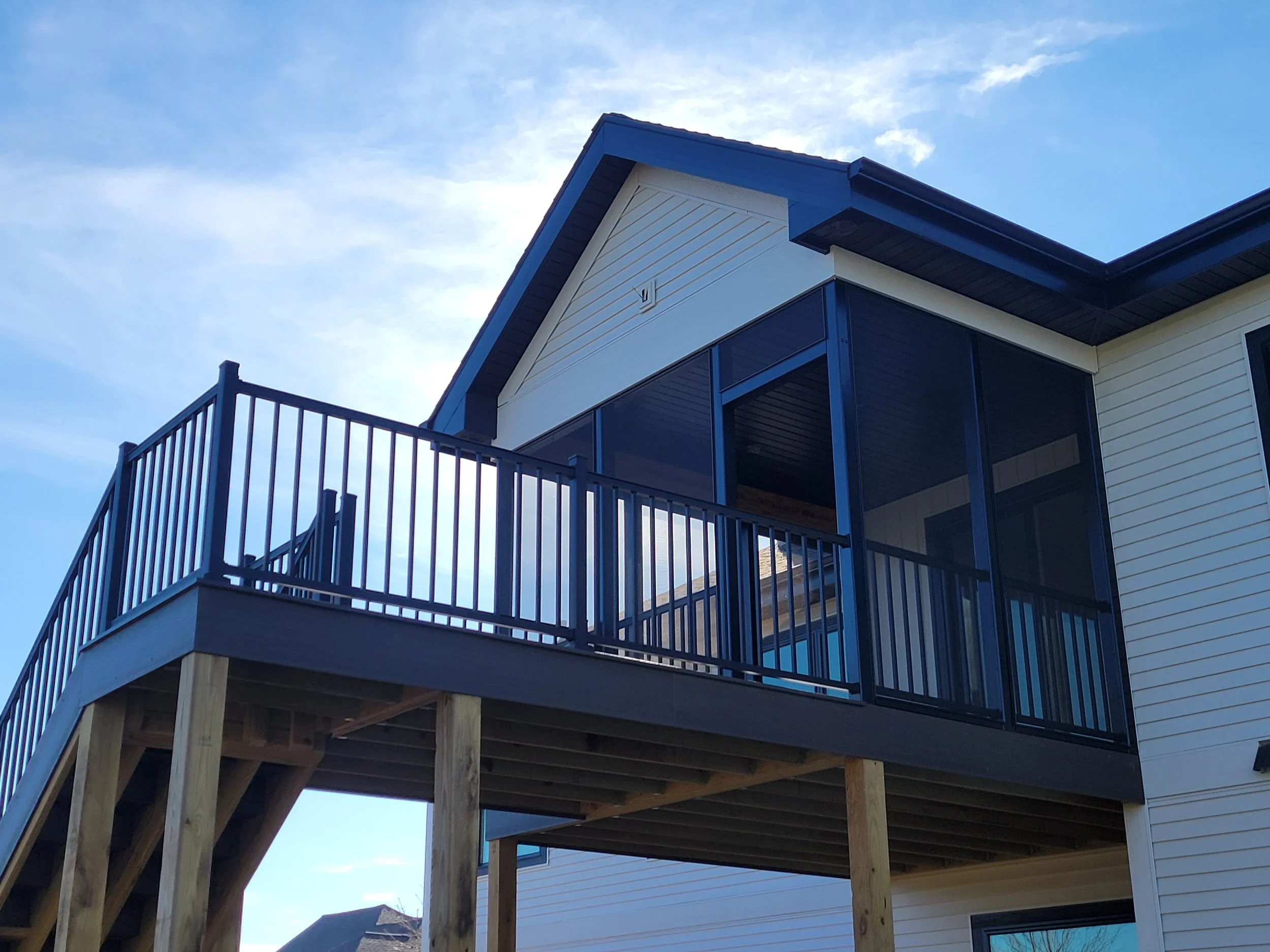 Modern house with an elevated covered porch with black metal railing, supported by wooden posts, under a clear blue sky.