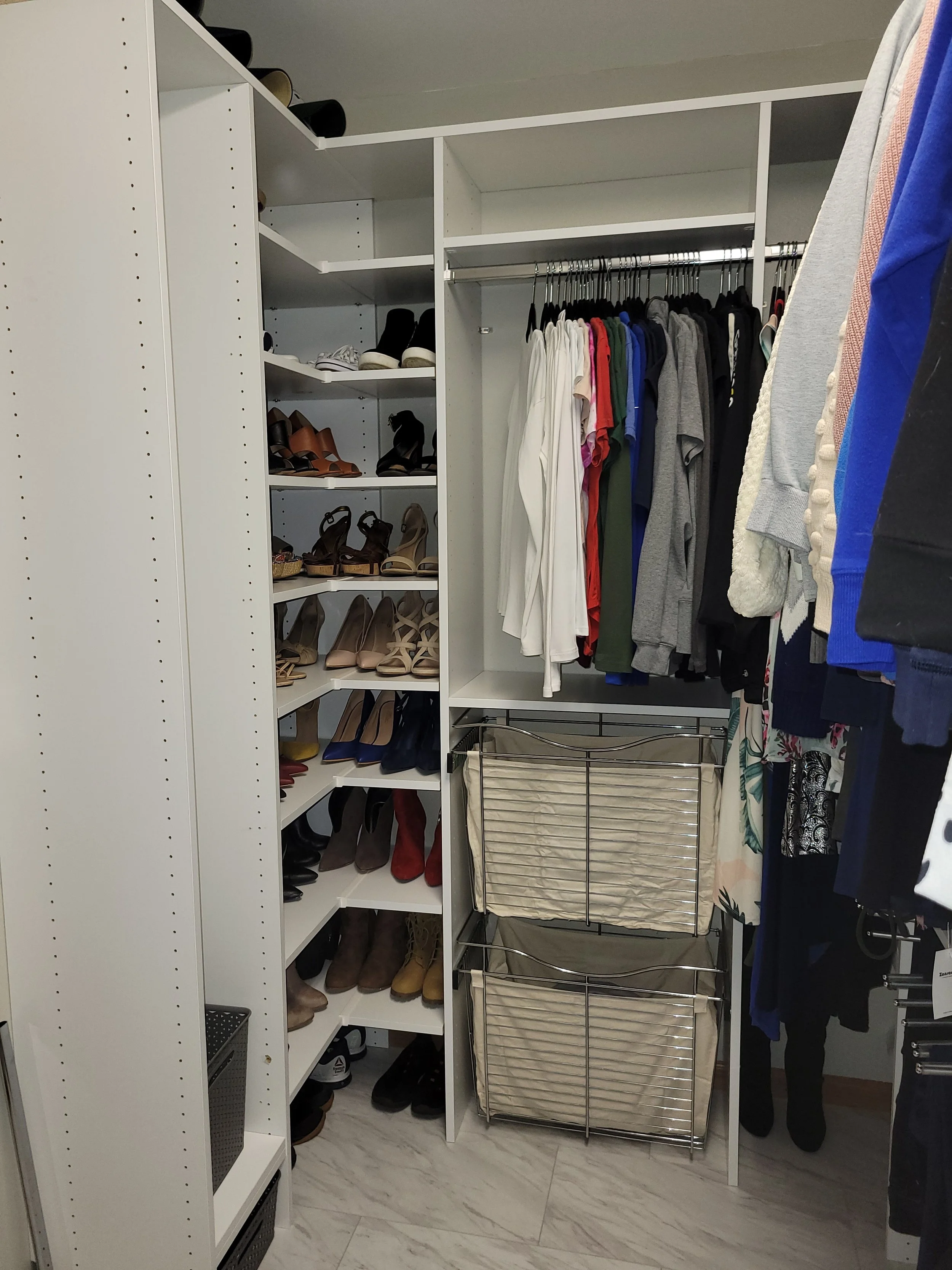 A walk-in closet with white shelves filled with shoes on the left, hanging clothes including shirts and dresses in the center, and beige fabric organizers with wire frames on the right side for additional storage.