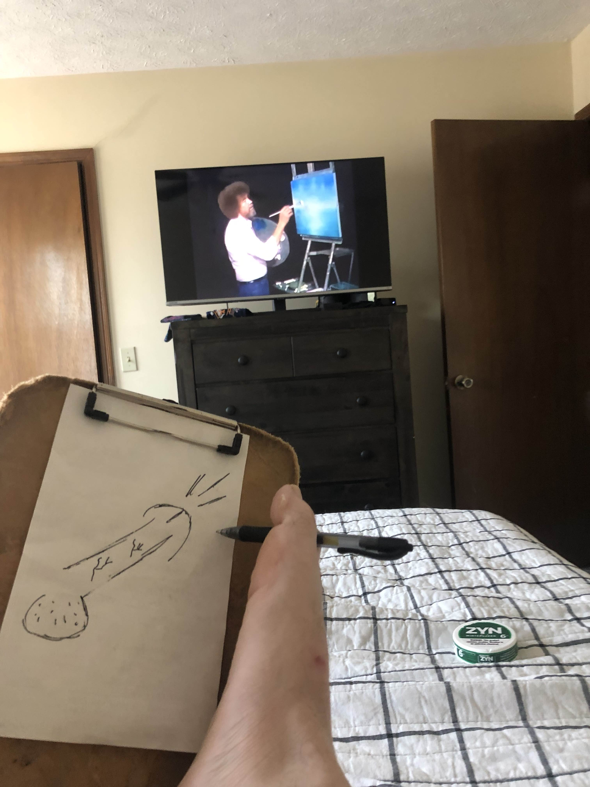 Person drawing a cylinder with their foot on a sketchpad, with a TV showing Bob Ross painting on a canvas in the background.