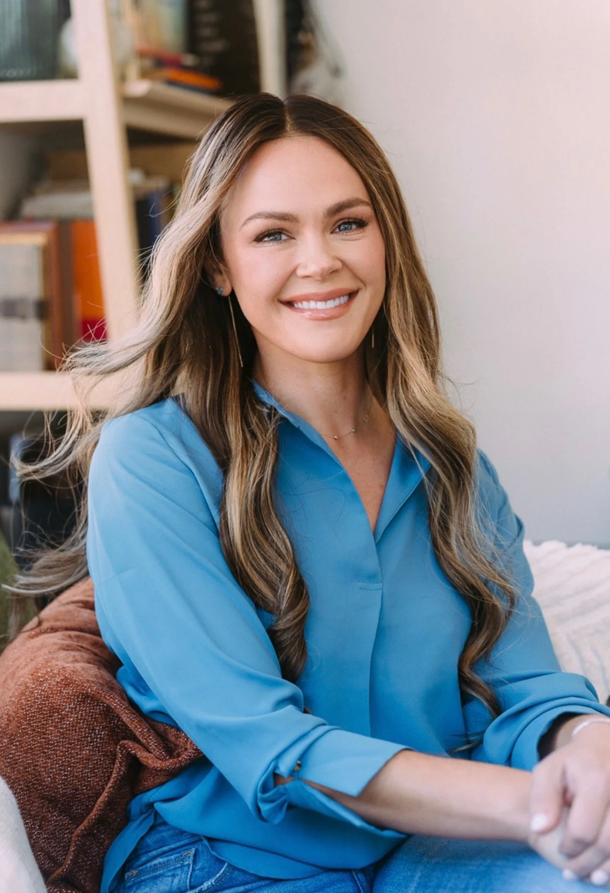 Svetlana Ishchenko of Vera Nova Therapy with long, wavy hair wearing a blue shirt, smiling while sitting indoors.