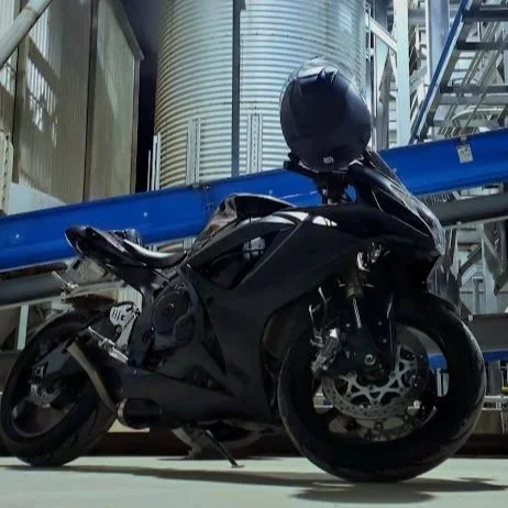 A black motorcycle parked indoors near industrial equipment with metal tanks and blue piping.