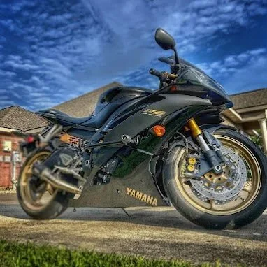Black Yamaha motorcycle parked on a driveway with a house and cloudy sky in the background.