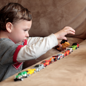 A young boy playing with toy cars lined up on a brown couch.
