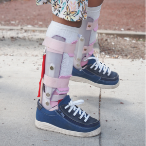 Person wearing orthopedic leg braces and navy sneakers on a sidewalk
